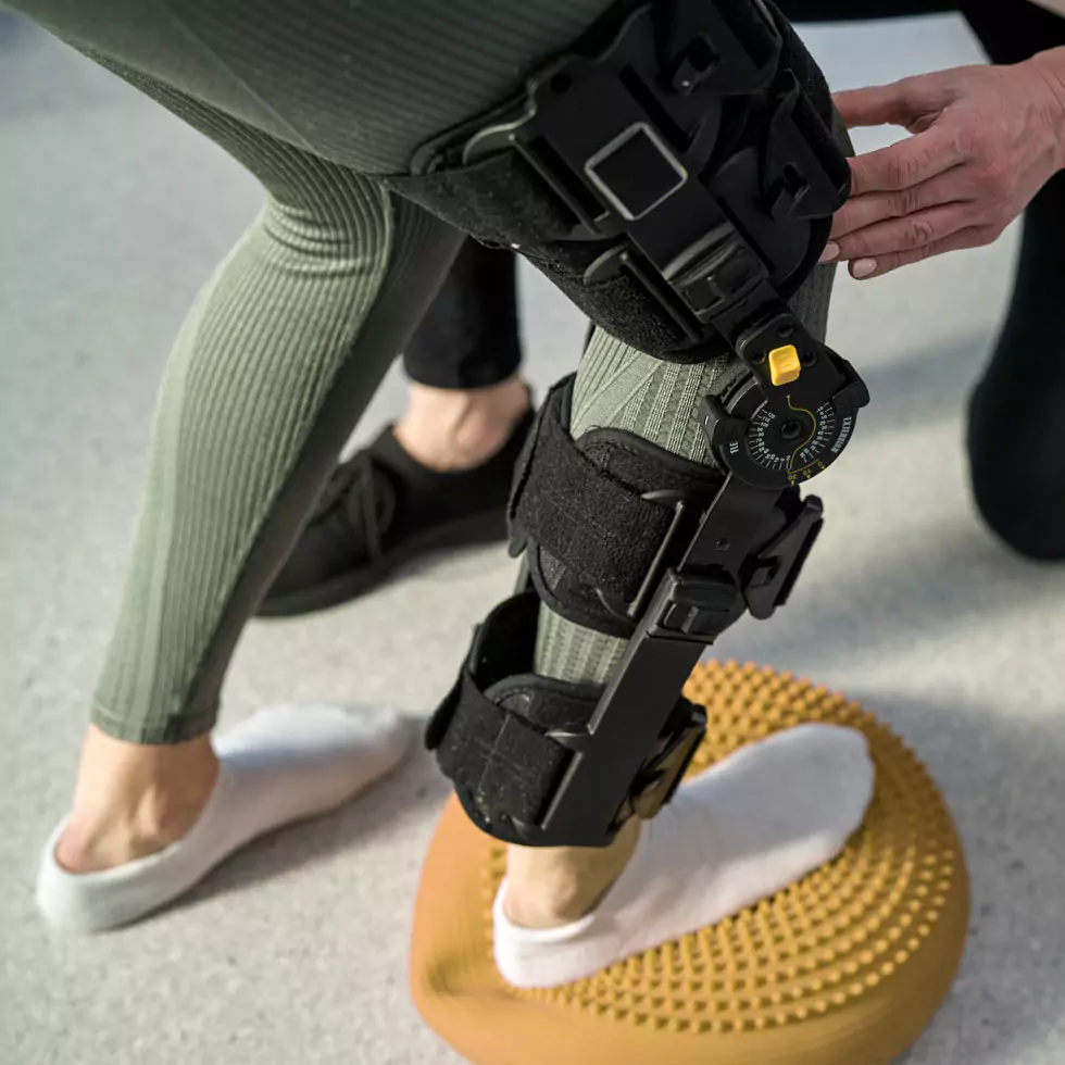 Physiotherapie verletztes Knie Junge Frau mit Orthese bei der Arbeit mit einem Physiotherapeuten