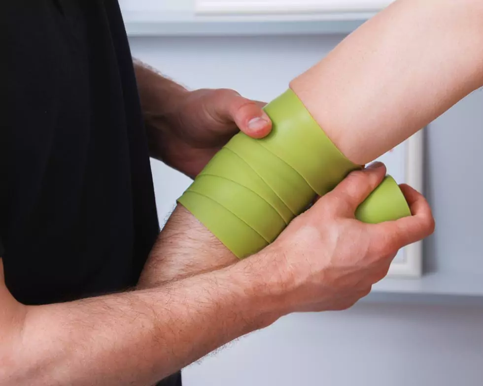 Therapeut bindet Flossingband um den Ellenbogen eines Patienten