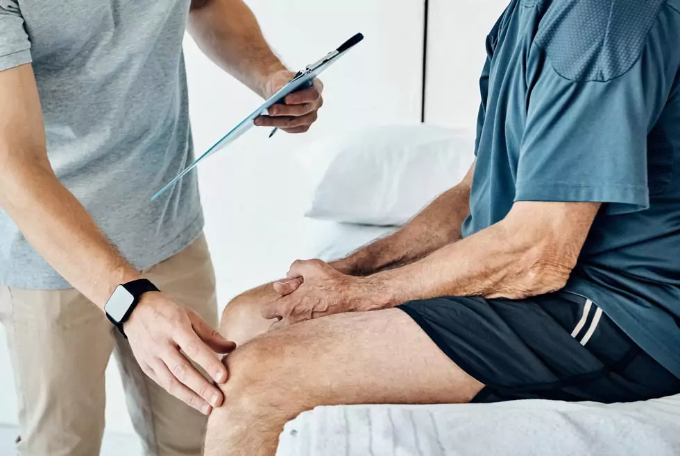 Untersuchung Knie Physiotherapeut untersucht das Knie eines älteren Patienten. Physiotherapeut hält die Patientenakte in der Hand