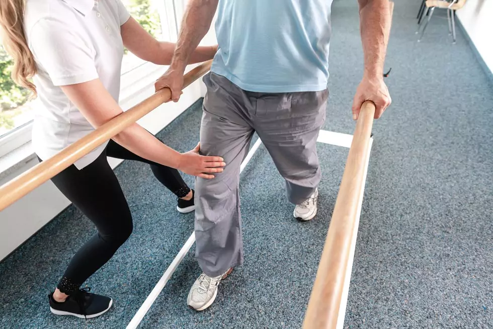 Krankengymnastik am Gerät Physiotherapeutin hilft älterem Mann in der Rehabilitation beim Gehen am Barren